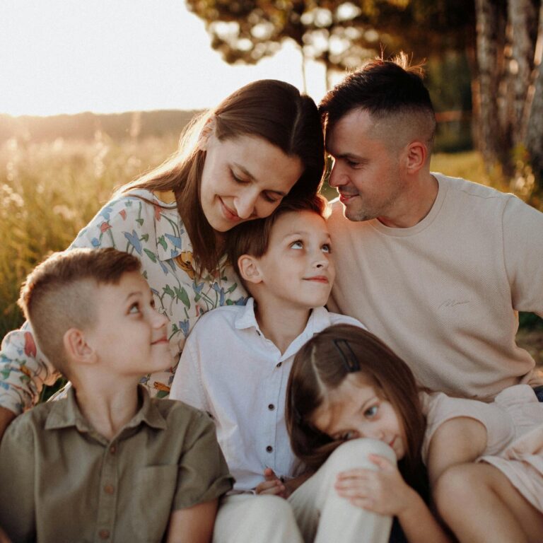 A joyful family of five sitting together, enjoying a warm sunset in the countryside.